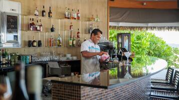 A bar area with a bartender, shelves of liquor bottles, and a counter with glasses and a coffee machine.