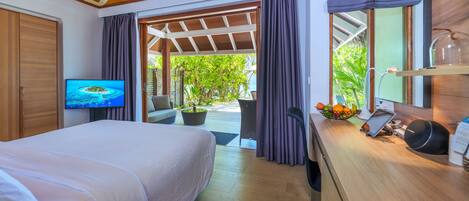 A bedroom with a bed, a TV, a desk with a computer, and a view of the outdoors.