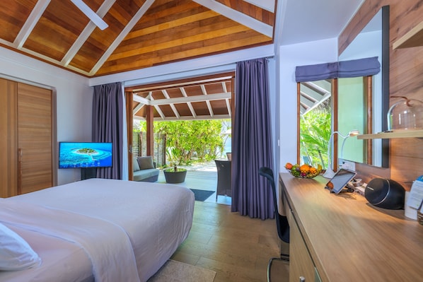 A bedroom with a bed, a TV, a desk with a computer, and a view of the outdoors. - Kandolhu Maldives (NORTH ARI ATOLL)