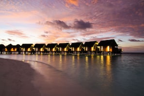 Una fila di bungalow sull'acqua sotto un cielo al tramonto.