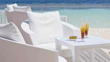 Zona de estar al aire libre con mesa y bebidas, con vistas a una playa y al océano.