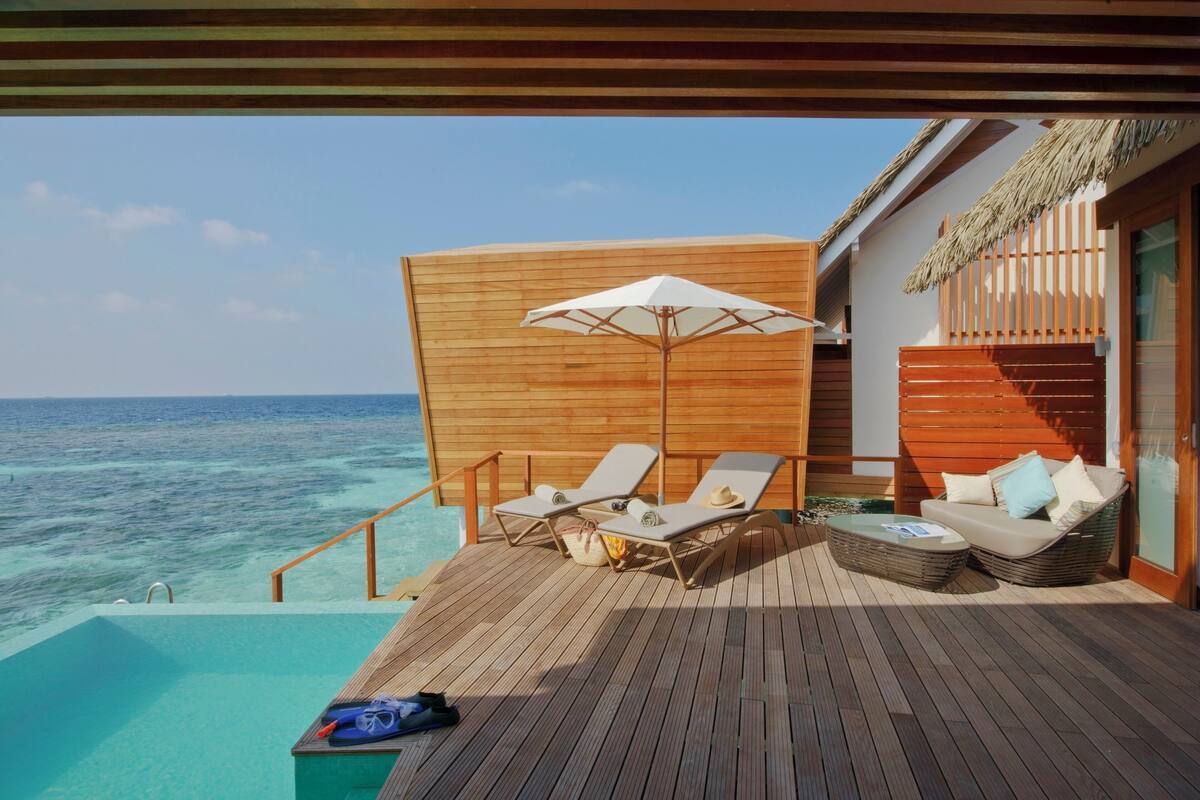 Una terraza de madera con sillones de descanso, una mesita y una sombrilla blanca con vista al océano.