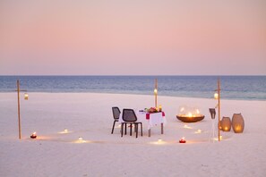Une table dressée pour un dîner sur la plage, avec des chaises, des bougies et des lanternes.