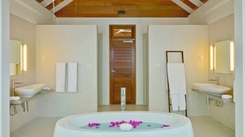 Un baño moderno con dos lavamanos, una bañera grande con pétalos de rosa y vigas de techo de madera.
