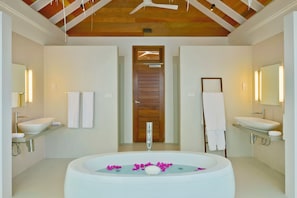 Un baño moderno con dos lavamanos, una bañera grande con pétalos de rosa y vigas de techo de madera.
