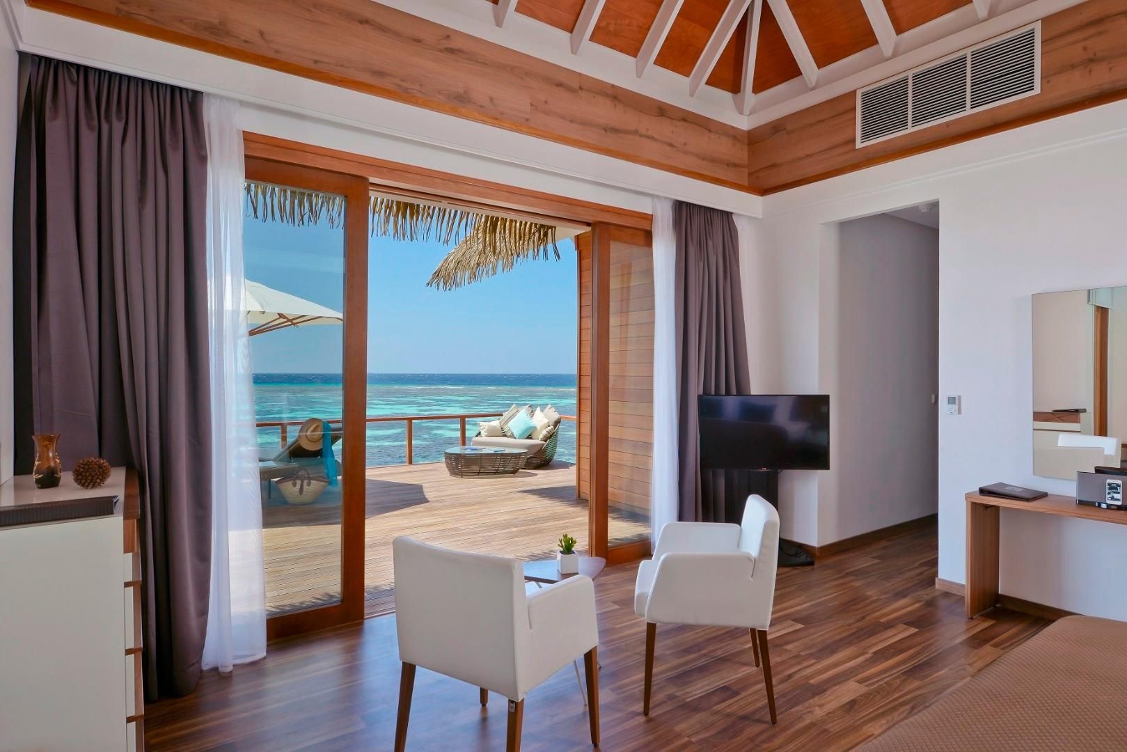 Una habitación con techo de madera, televisión, escritorio y vistas al océano.