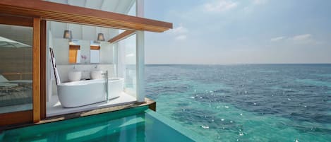 Una piscina infinita con vistas al océano, un baño moderno con bañera y una terraza de madera.