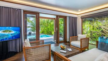 A modern hotel room with a TV, wicker furniture, a dining table, and a view of a pool and greenery.