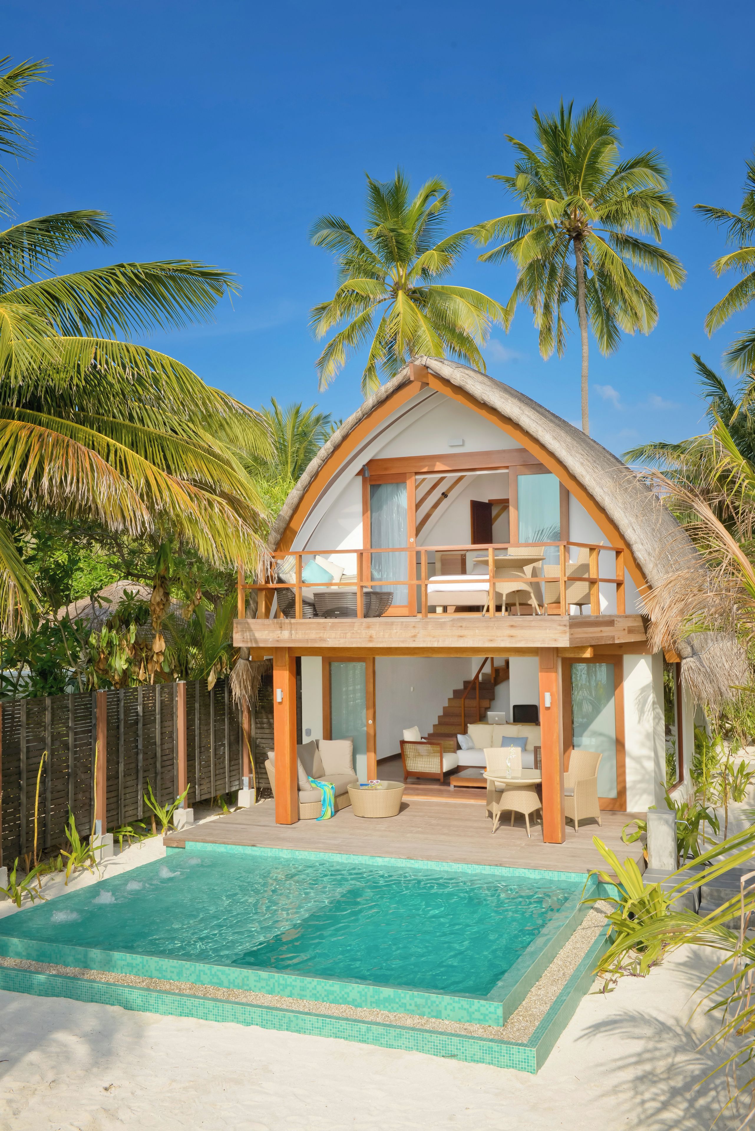 Una casa de dos pisos con piscina, rodeada de palmeras.