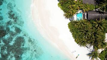 Vista aérea de una playa con aguas turquesas cristalinas, arena blanca y exuberantes palmeras.