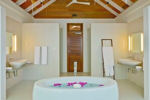 A modern bathroom with two sinks, a large bathtub with rose petals, and wooden ceiling beams. - Kandolhu Maldives (NORTH ARI ATOLL)