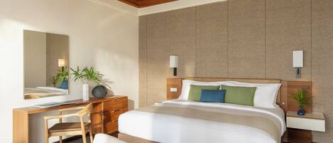 A modern hotel room with a large bed, a desk, a chair, and a bedside table with a lamp.