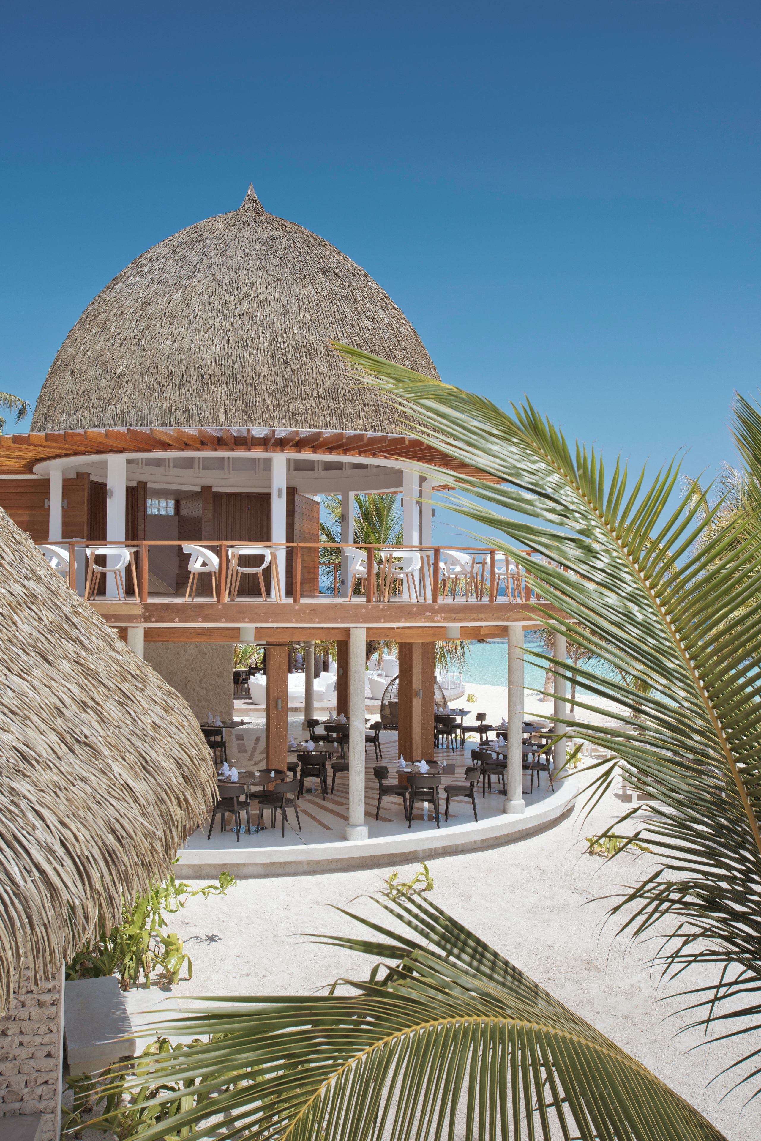 Un resort con una estructura de techo de paja, asientos al aire libre y vista a la playa.