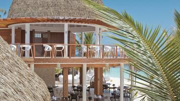 Un resort con una estructura de techo de paja, asientos al aire libre y vista a la playa.