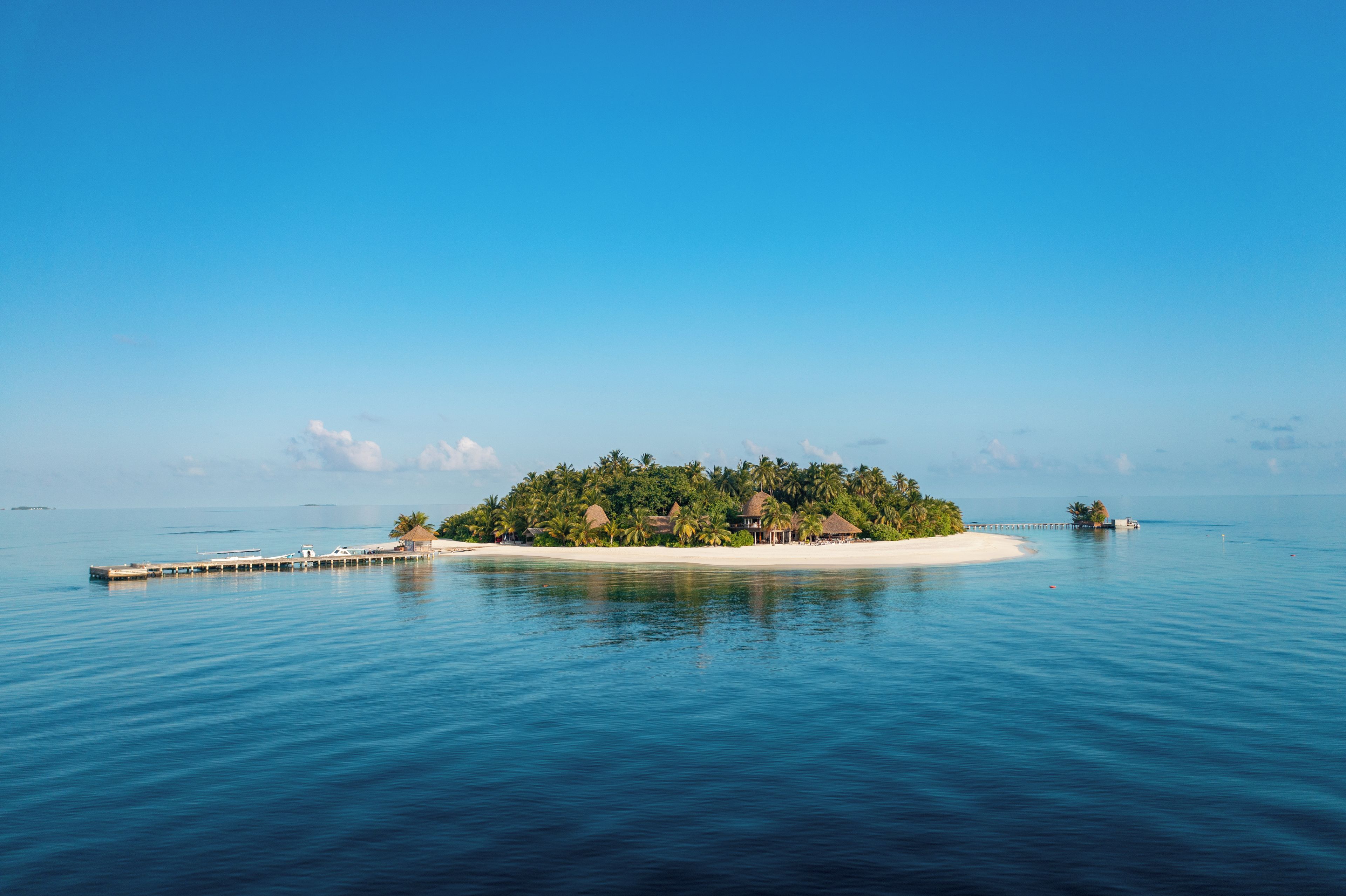 A tropical island with a pier extending into calm blue waters, surrounded by lush greenery and palm trees.