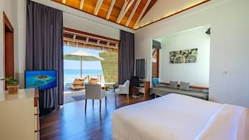 A modern hotel room with a large bed, a desk with a chair, a TV, and a view of the ocean.