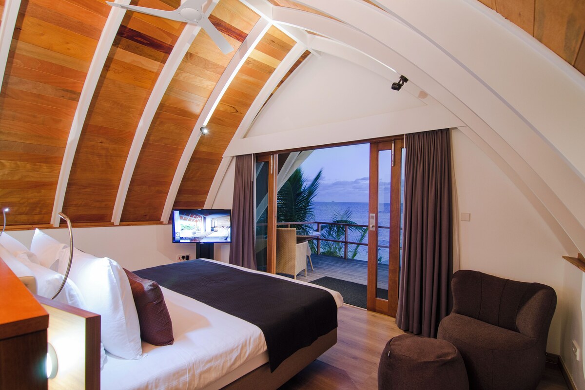 Une chambre avec un lit, une télévision et un balcon donnant sur la mer.
