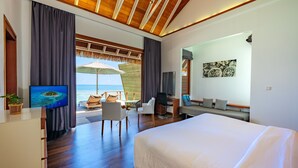 A modern hotel room with a large bed, a desk with a chair, a TV, and a view of the ocean. - Kandolhu Maldives (NORTH ARI ATOLL)