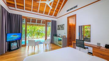 A modern hotel room with a large bed, a desk, a chair, a television, and a view of a pool and greenery.