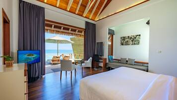 Una habitación de hotel moderna con una cama grande, un escritorio con silla, un televisor y vista al océano.