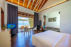 A modern hotel room with a large bed, a desk with a chair, a TV, and a view of the ocean. - Kandolhu Maldives (NORTH ARI ATOLL)