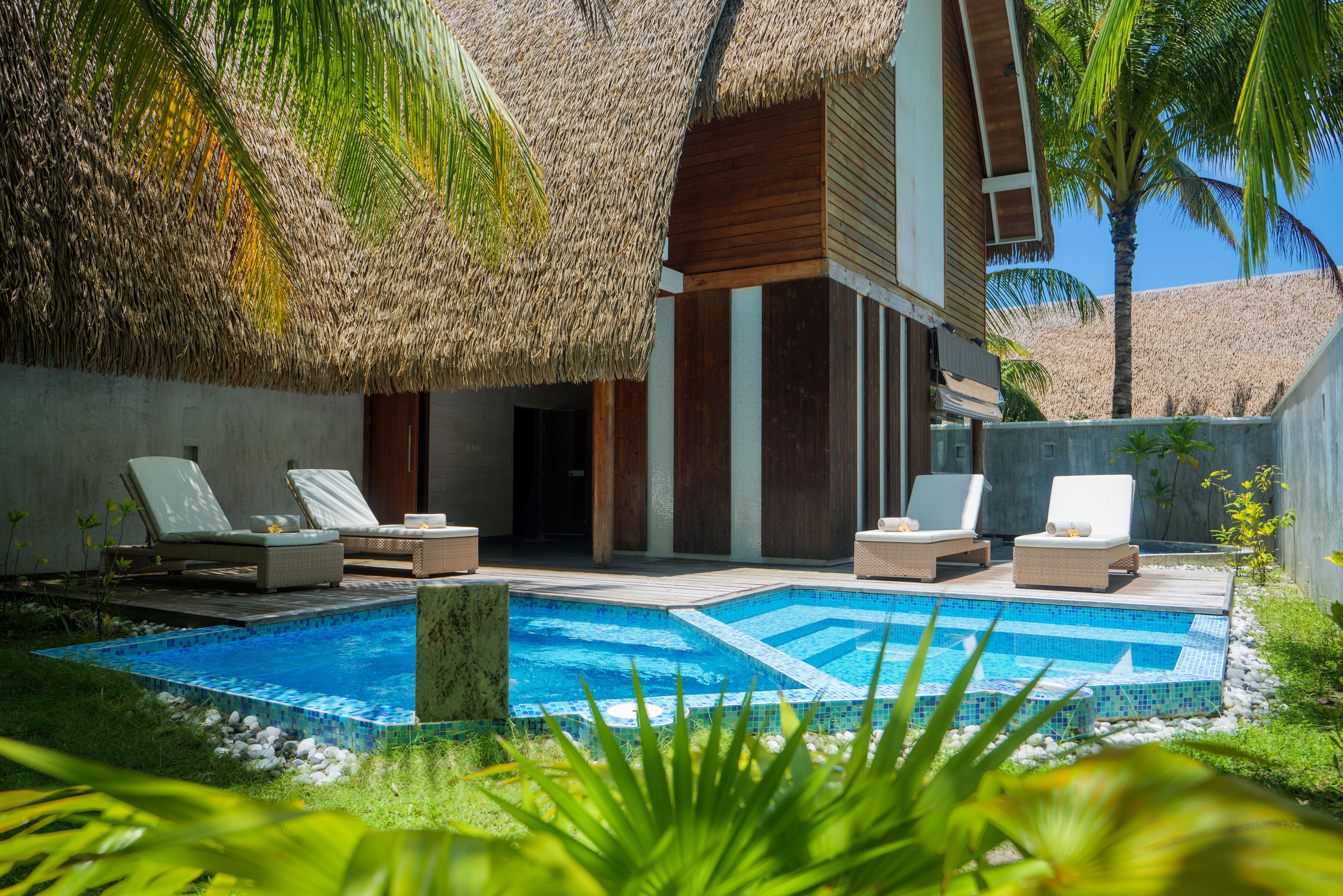 Un área de piscina con sillas de descanso y una estructura de techo de paja.