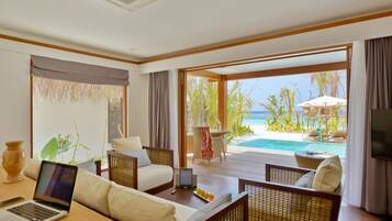 Habitación de hotel con una laptop sobre una mesa, un sofá y vista a una piscina y una playa.