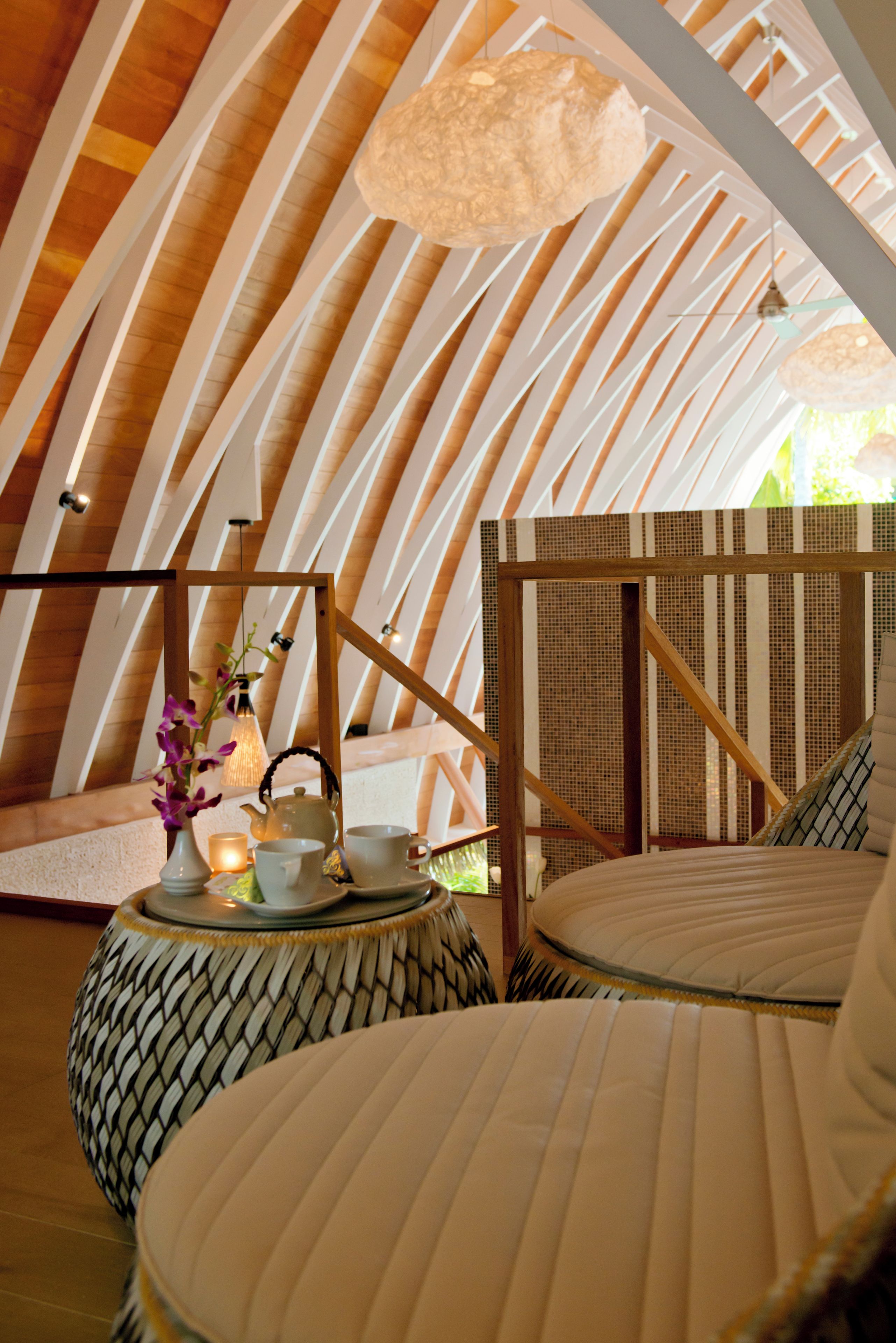 Un espacio circular y acogedor con techo de madera y una lámpara colgante. Hay una pequeña mesa con un hervidor, tazas y una vela. El ambiente ofrece una zona de estar confortable con cojines.