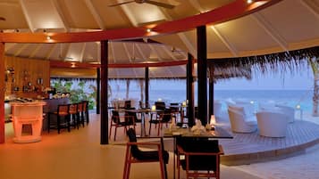 Un restaurante frente al mar, con vistas al océano, mesas, sillas y una zona de bar.