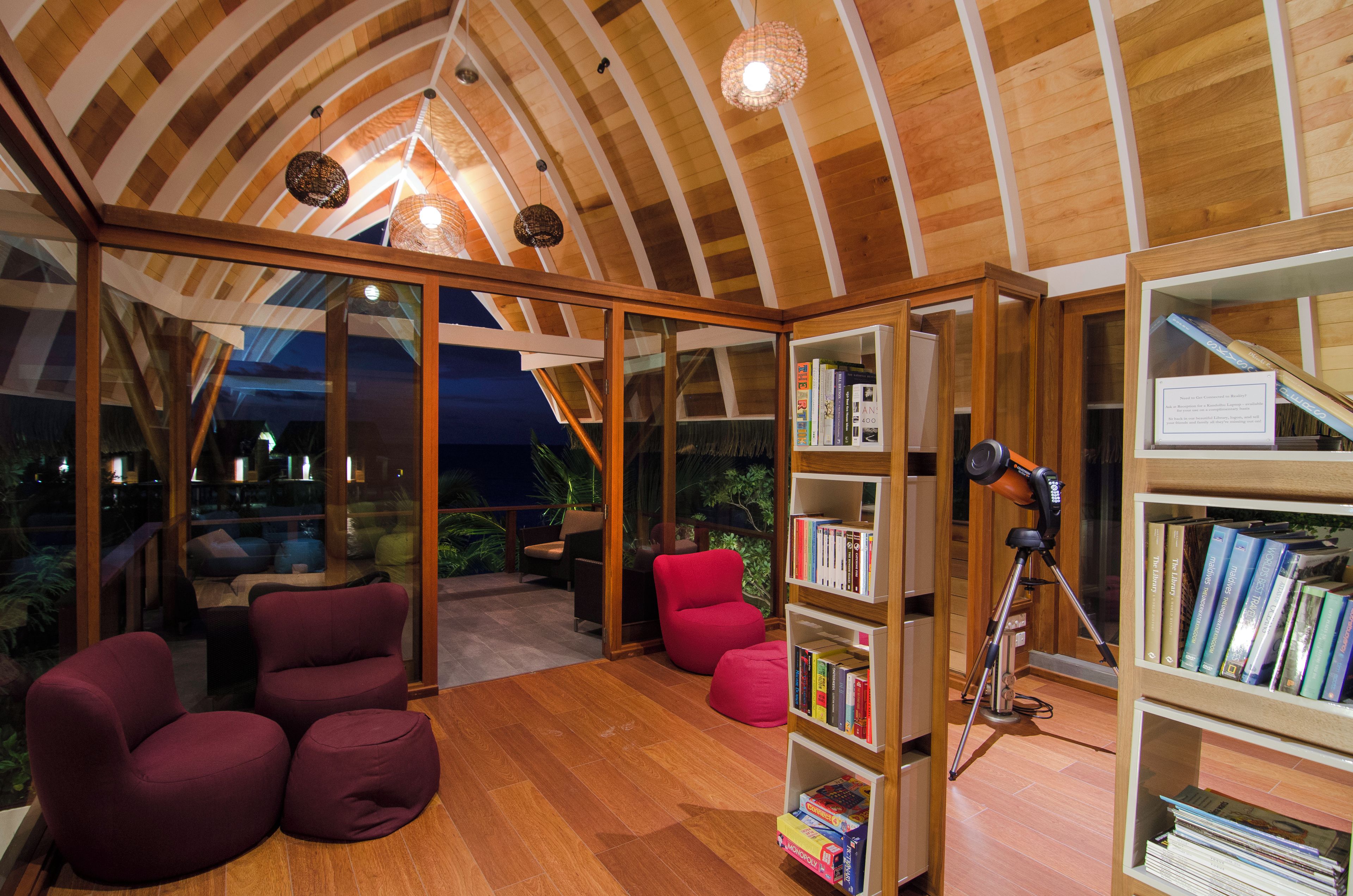 Una sala de lectura acogedora con estanterías de madera, asientos cómodos y un techo con vigas de madera.