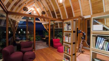 Una sala de lectura acogedora con estanterías de madera, asientos cómodos y un techo con vigas de madera.