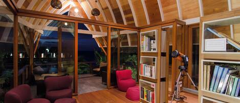 A cozy reading room with wooden bookshelves, comfortable seating, and a ceiling with wooden beams.