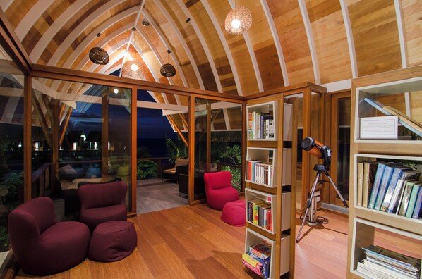 A cozy reading room with wooden bookshelves, comfortable seating, and a ceiling with wooden beams. - Kandolhu Maldives (NORTH ARI ATOLL)