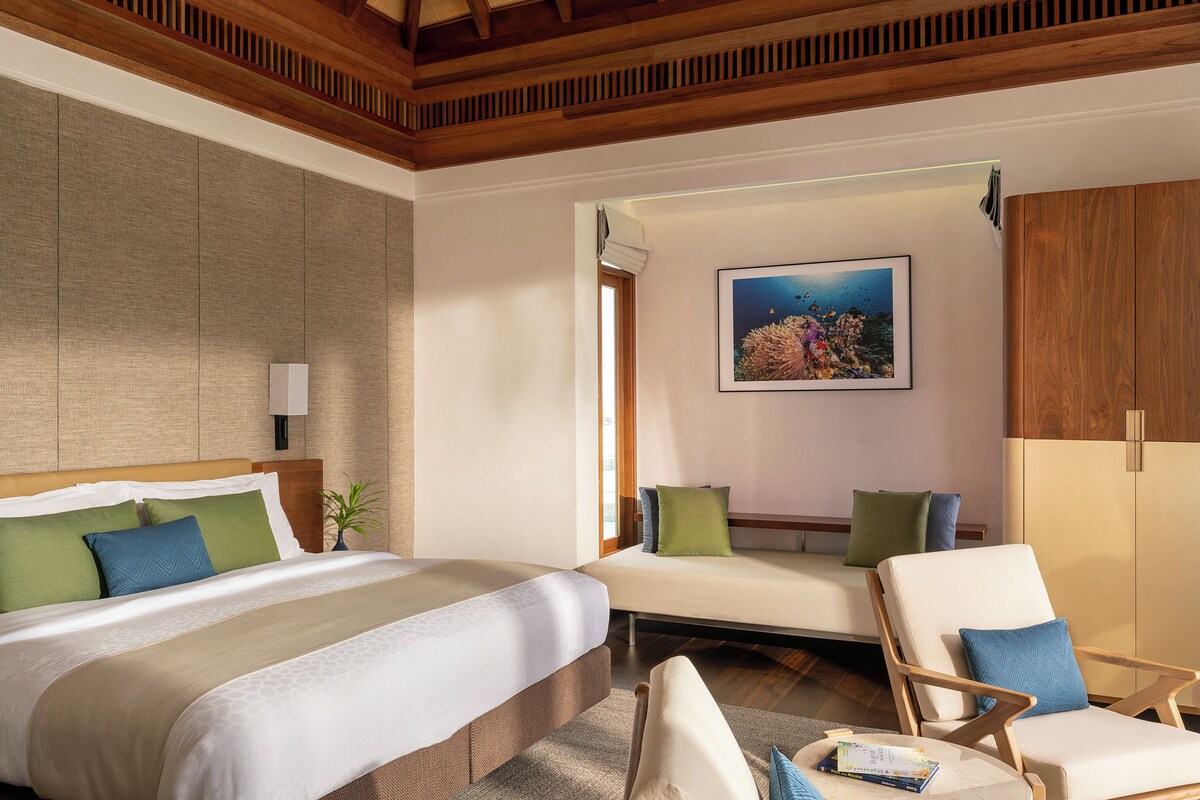 Une chambre d’hôtel avec un grand lit, un canapé, un fauteuil, un tableau et un plafond en bois.