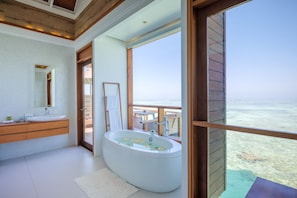 Un baño moderno con una bañera grande, un tocador con espejo y vistas al océano a través de un amplio ventanal.