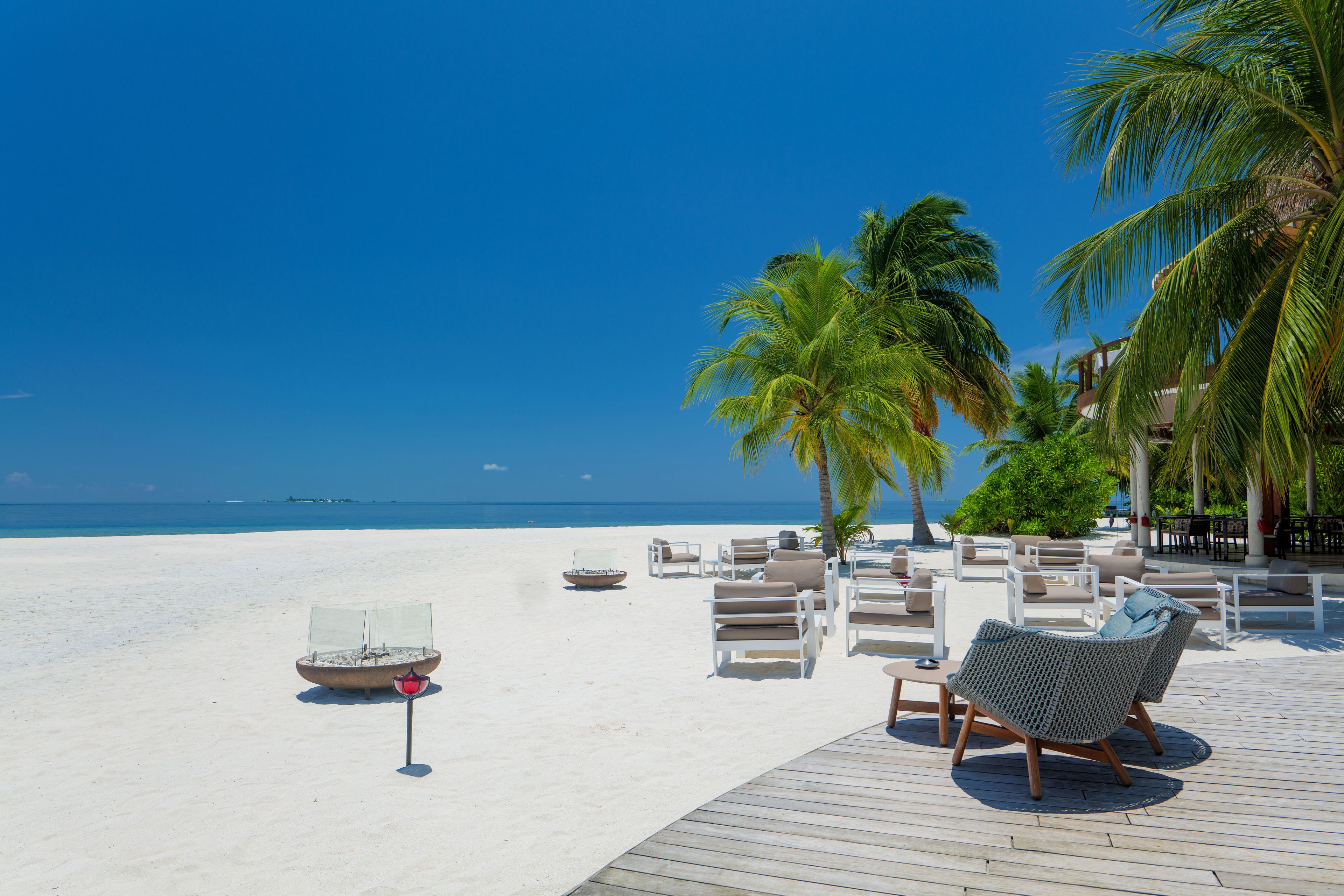 A beachside lounge with lounge chairs and a fire pit, overlooking the ocean.