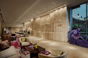 A spacious lobby with a high ceiling, a seating area with sofas and chairs, a coffee table with decorative items, and a large window with a view of greenery. - Ascott Kuningan Jakarta (Jakarta)