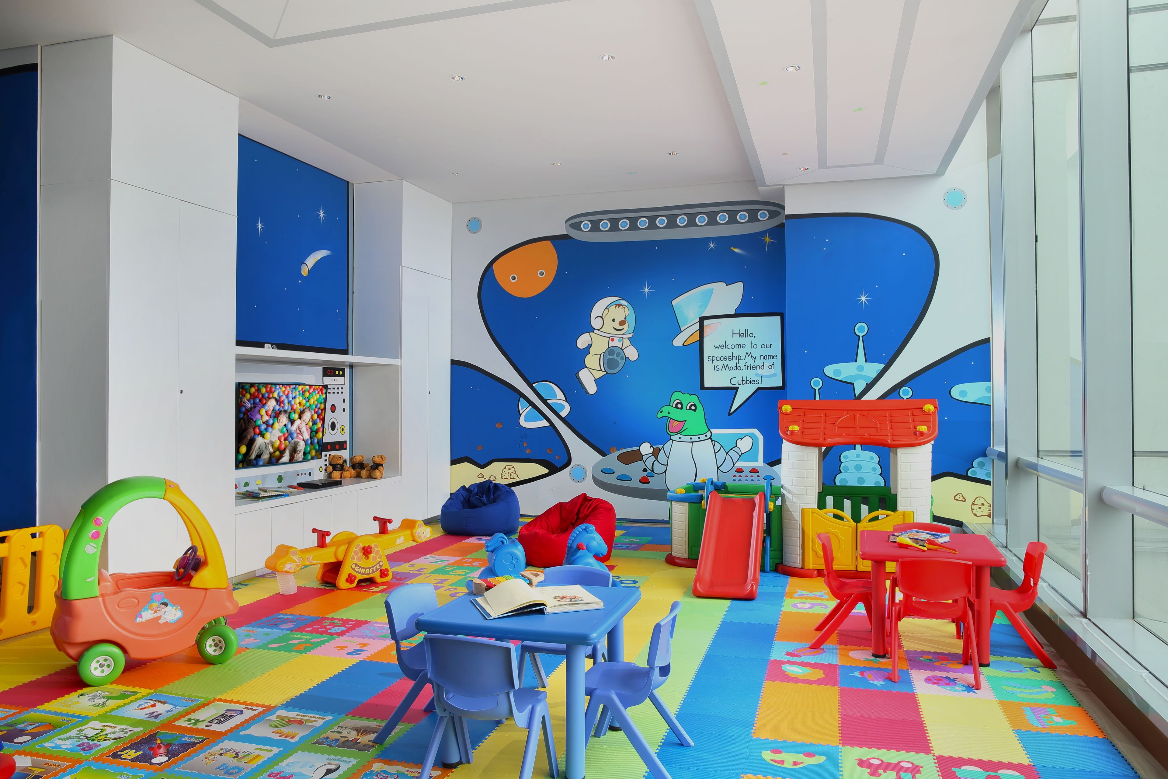 Un cuarto de juegos infantil con piso colorido, una cocina de juguete y decoración con temática espacial.
