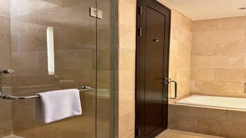 A modern bathroom with a glass-enclosed shower, a dark wooden door, and a white bathtub.