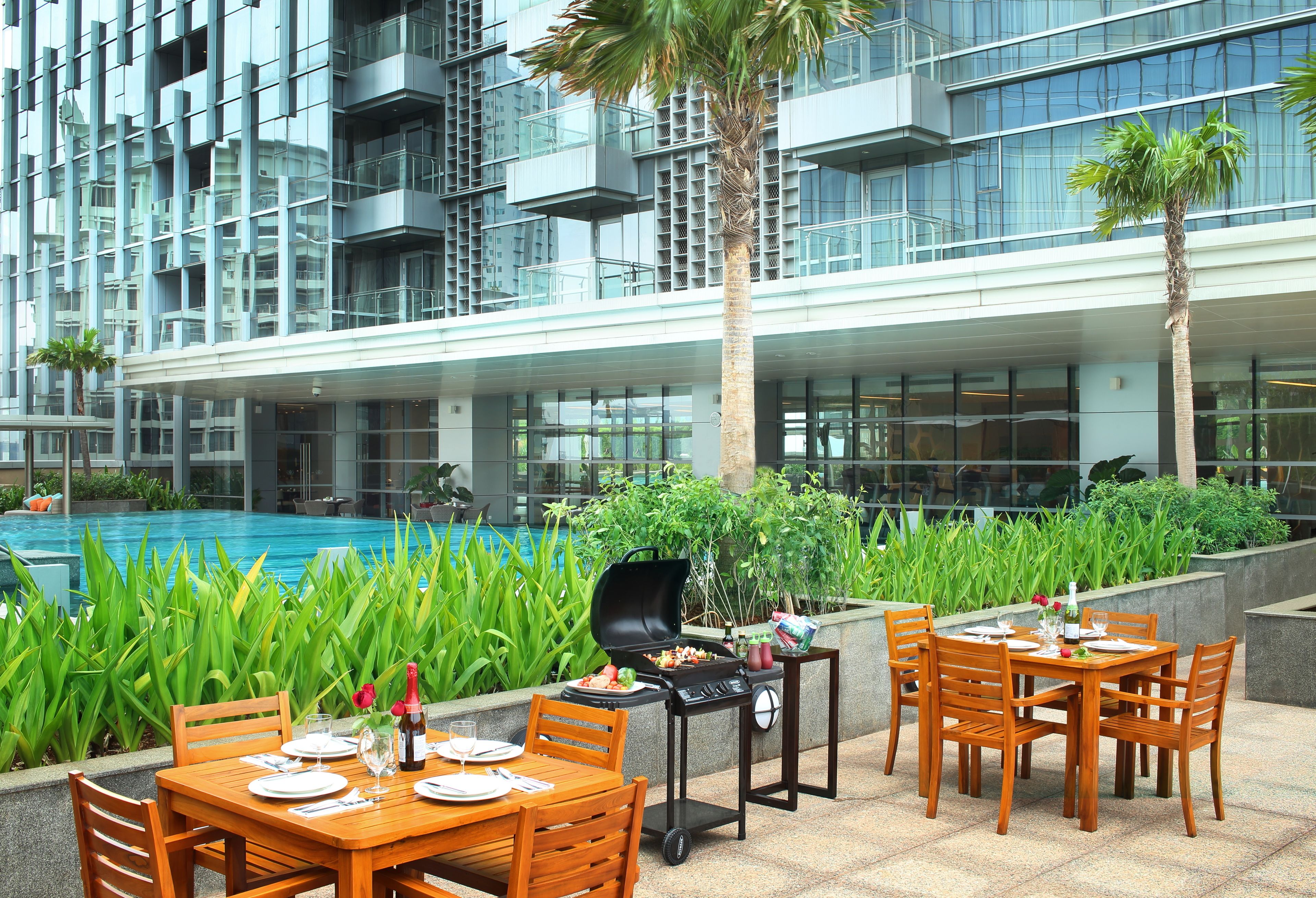 Un área de comedor al aire libre con una parrilla, mesas, sillas y una piscina al fondo.
