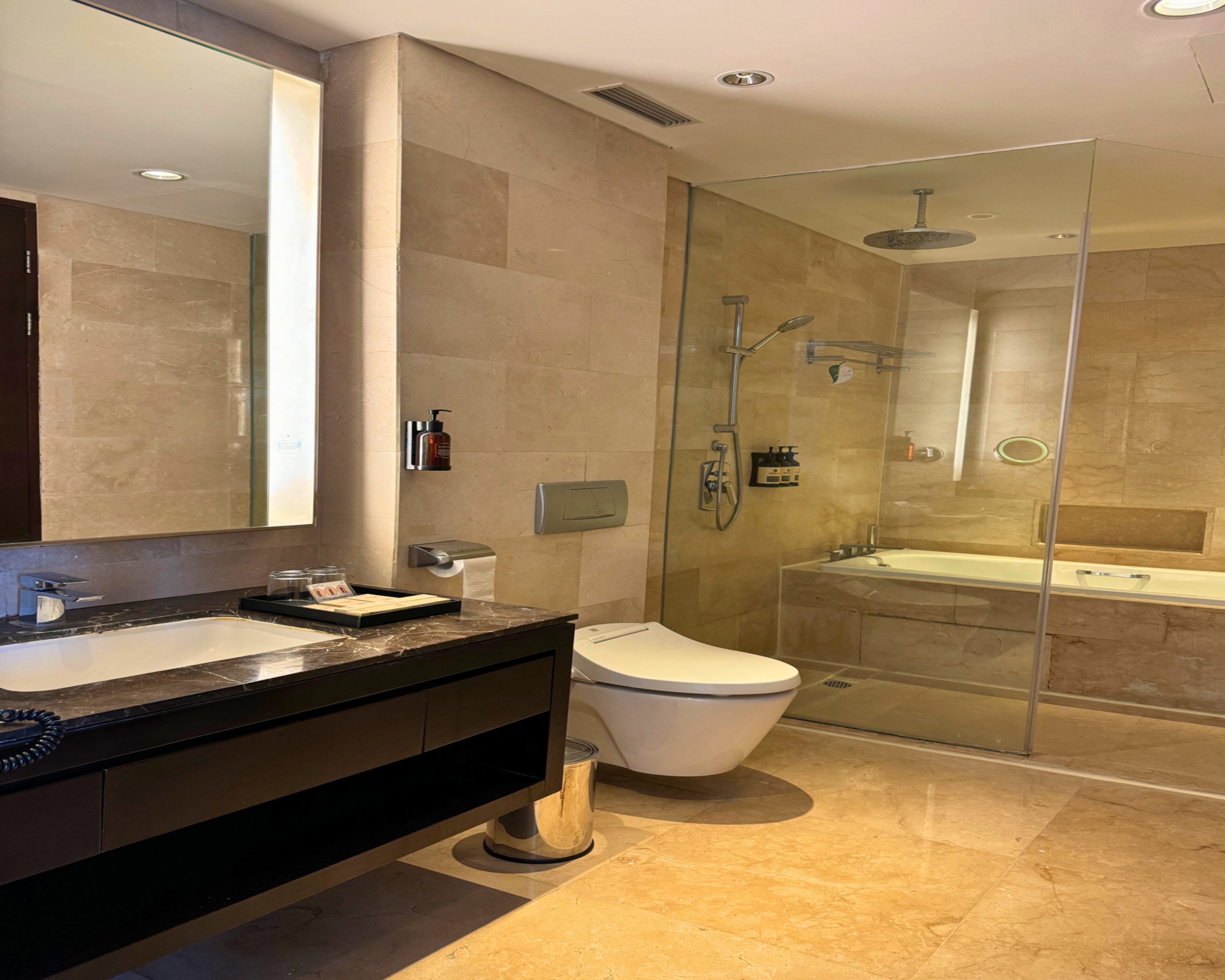 Un baño moderno con un espejo grande, una bañera, una ducha y un inodoro.