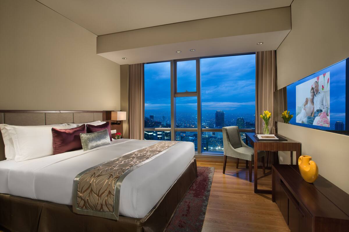 Une chambre d’hôtel moderne, dotée d’un grand lit, d’un bureau et offrant une vue sur le paysage urbain.