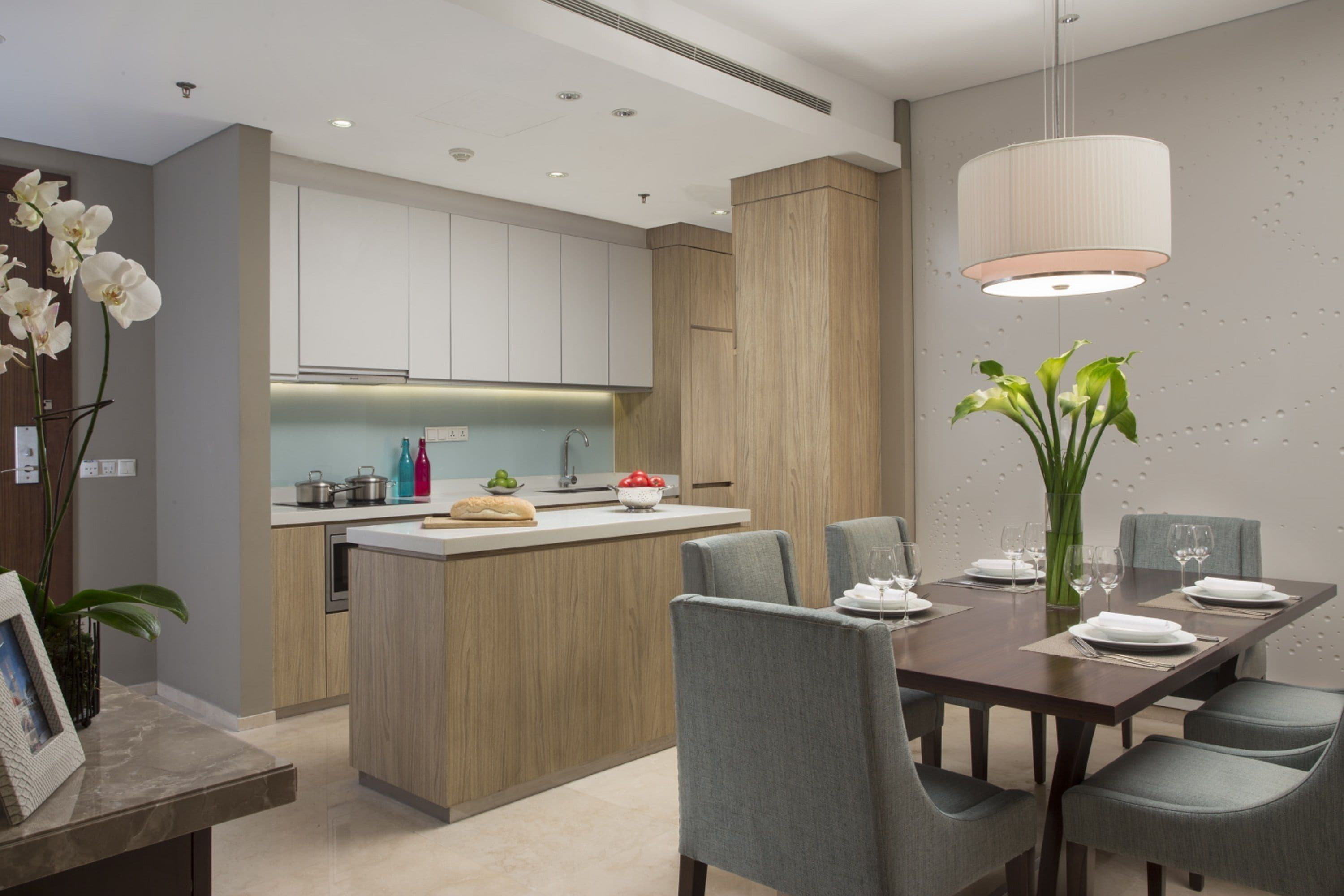 A modern kitchen with a central island, grey upholstered chairs, and a dining table set for six.