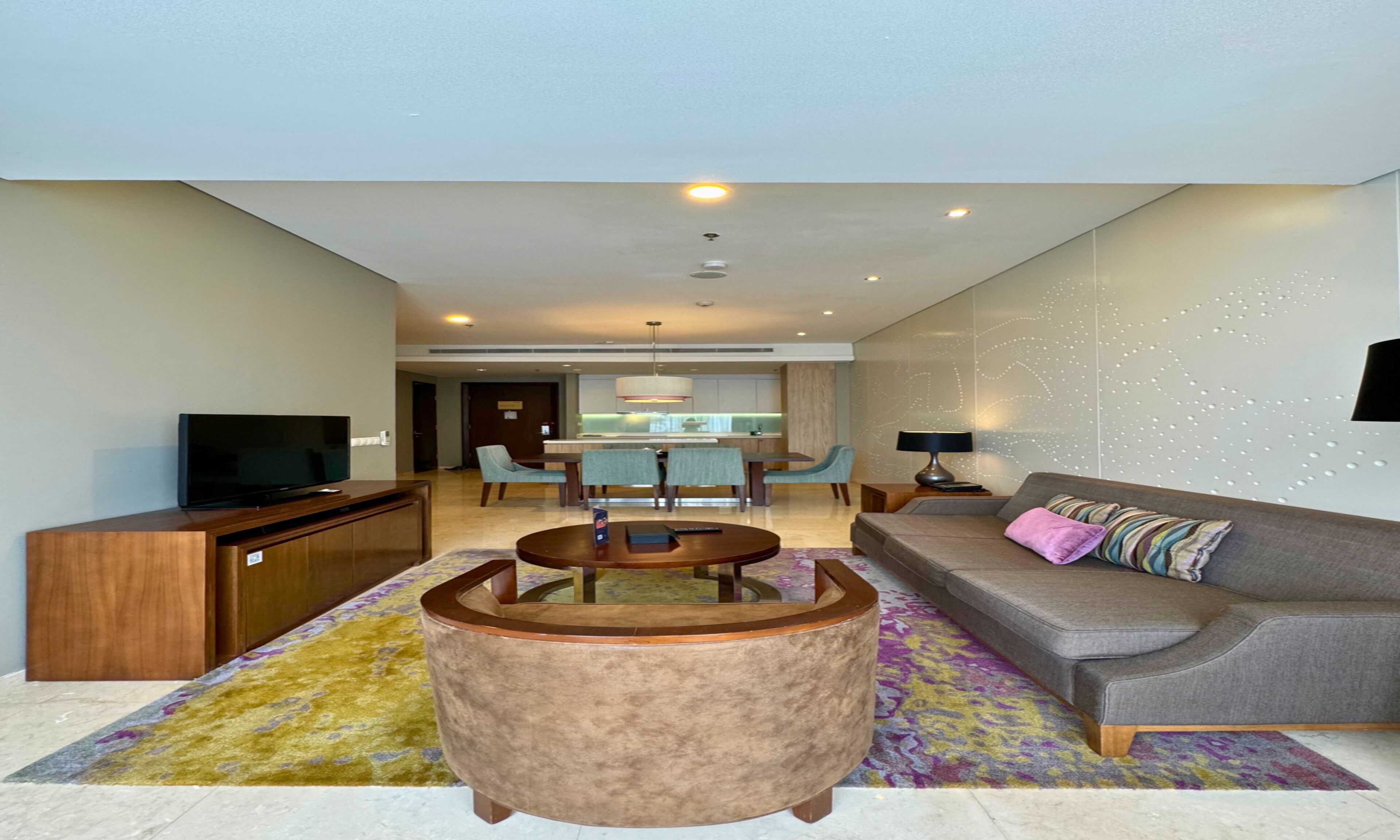A modern living room with a sofa, coffee table, TV, and a dining area with chairs and a table.