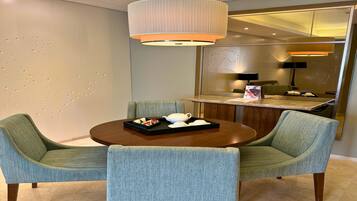 Un espace repas moderne avec une table ronde, deux chaises rembourrées, un mur décoratif orné d’un motif, un luminaire suspendu et un miroir qui reflète la pièce.