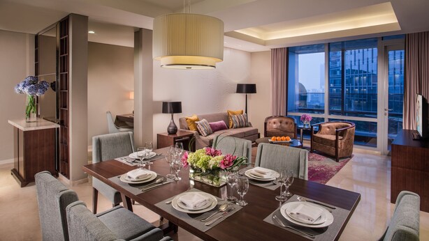 A modern dining area with a large table set for a meal, a sofa, and a view of the city through large windows. - Ascott Kuningan Jakarta (Jakarta)