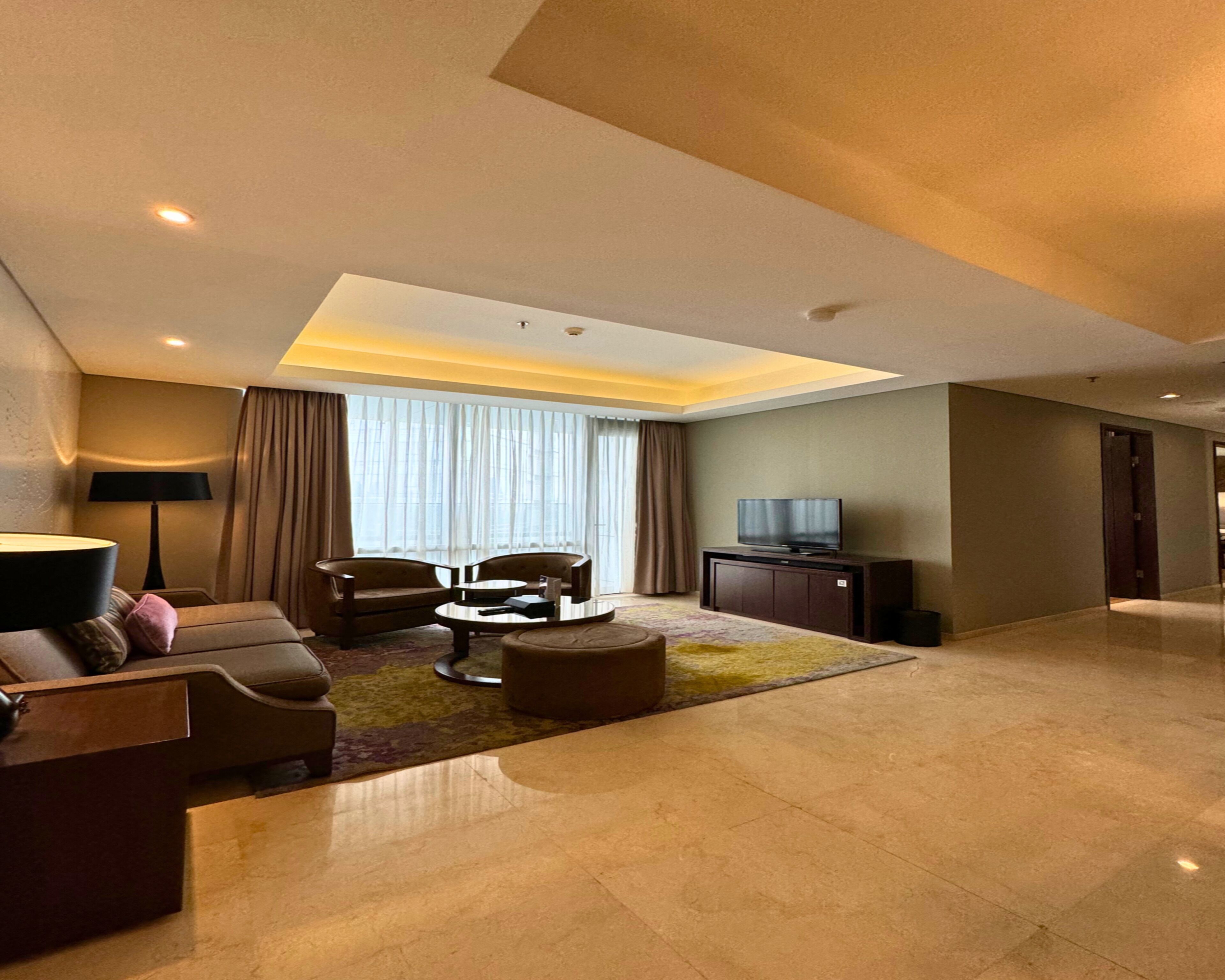 A modern living room with a sofa, chairs, a coffee table, a TV, and a large window with curtains.