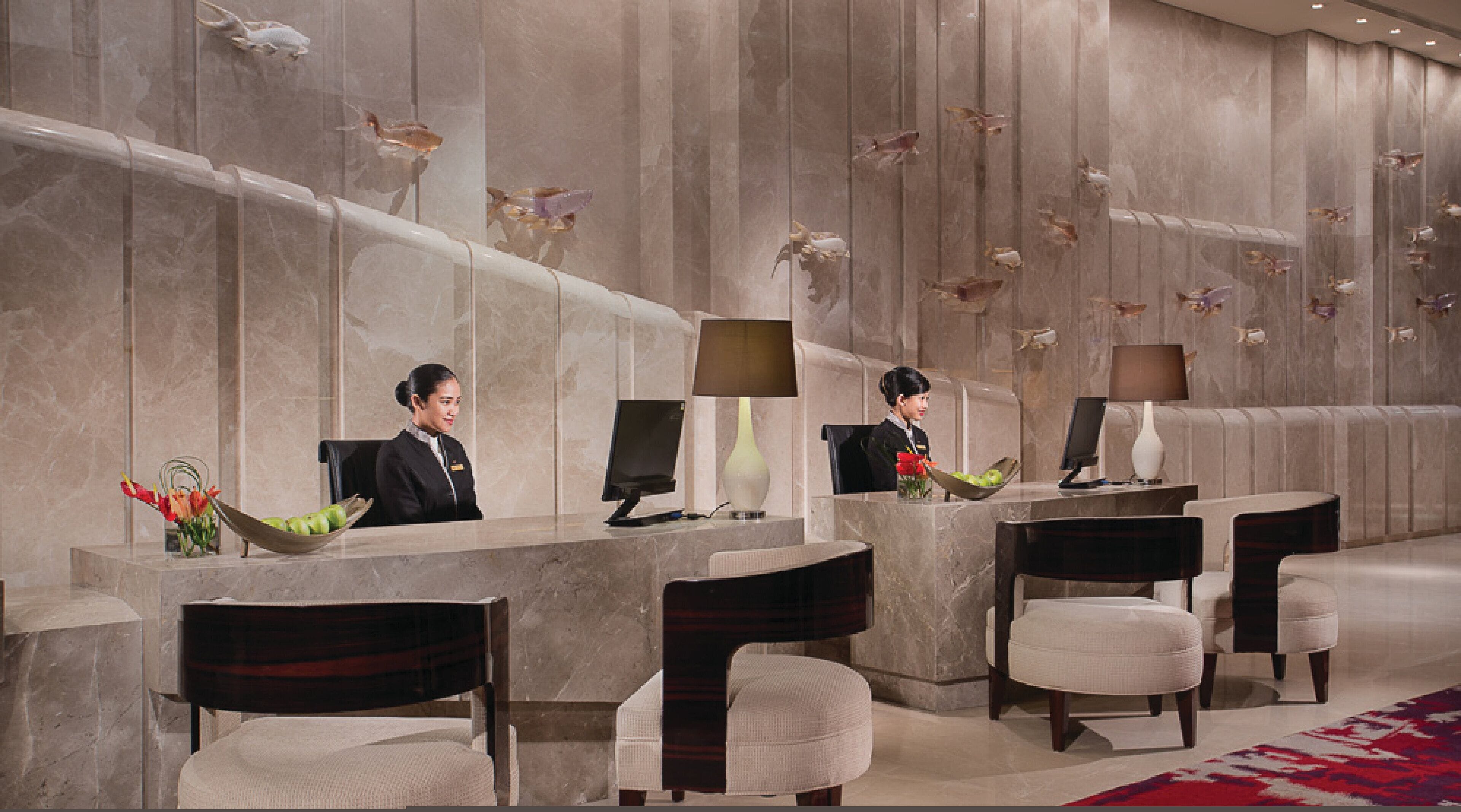 A hotel reception area with marble walls, two receptionists, and a modern desk setup.