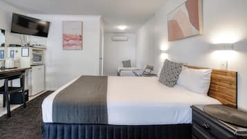 Habitación de hotel con cama, mesita de noche, televisión, kitchenette y un cuadro en la pared.