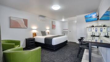 A hotel room with a bed, bedside tables, a desk, a chair, a flat-screen TV, and a wall-mounted air conditioning unit.